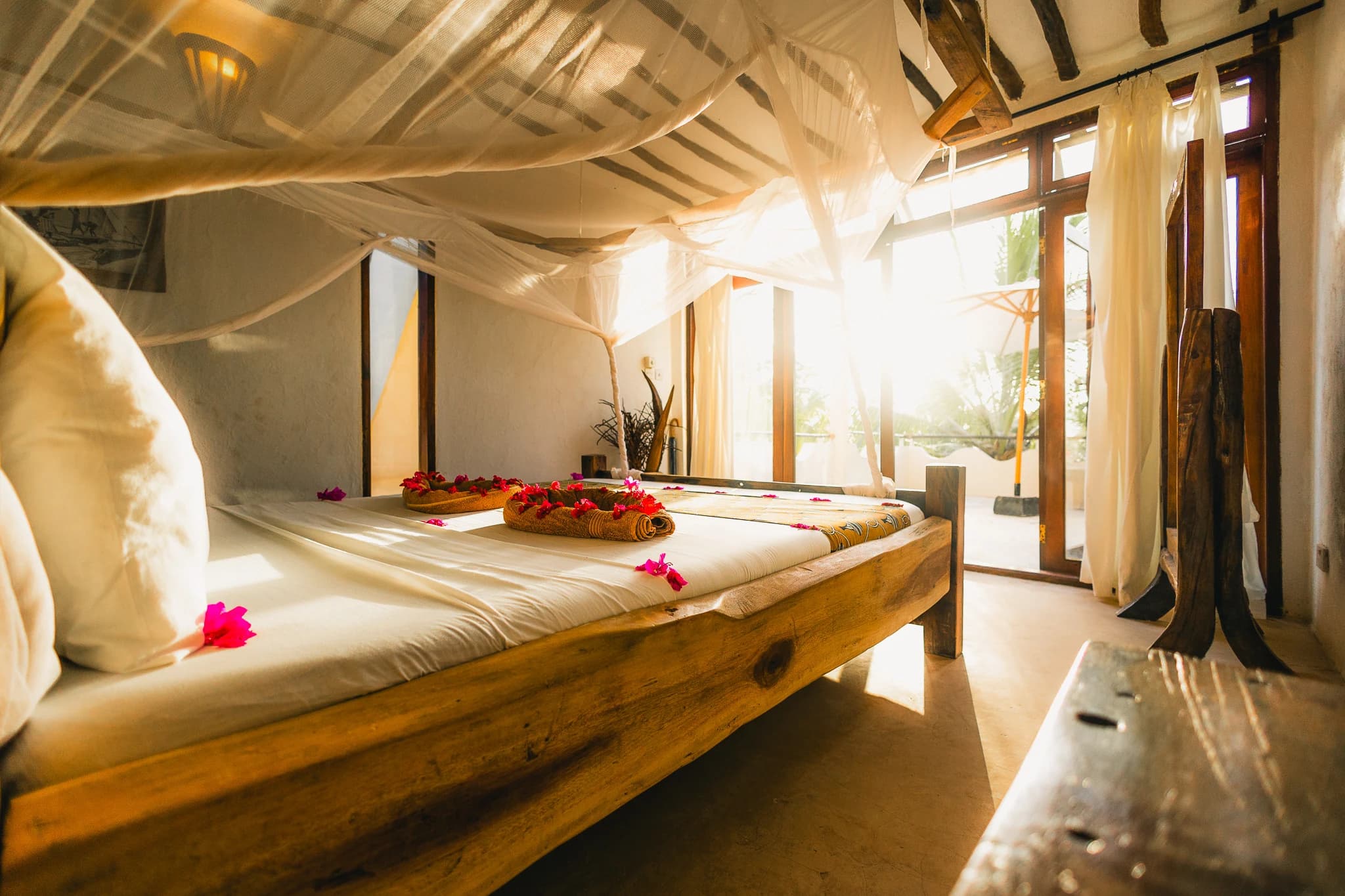Sunlit bedroom with a wooden bed and flowing canopy at Milele Villas