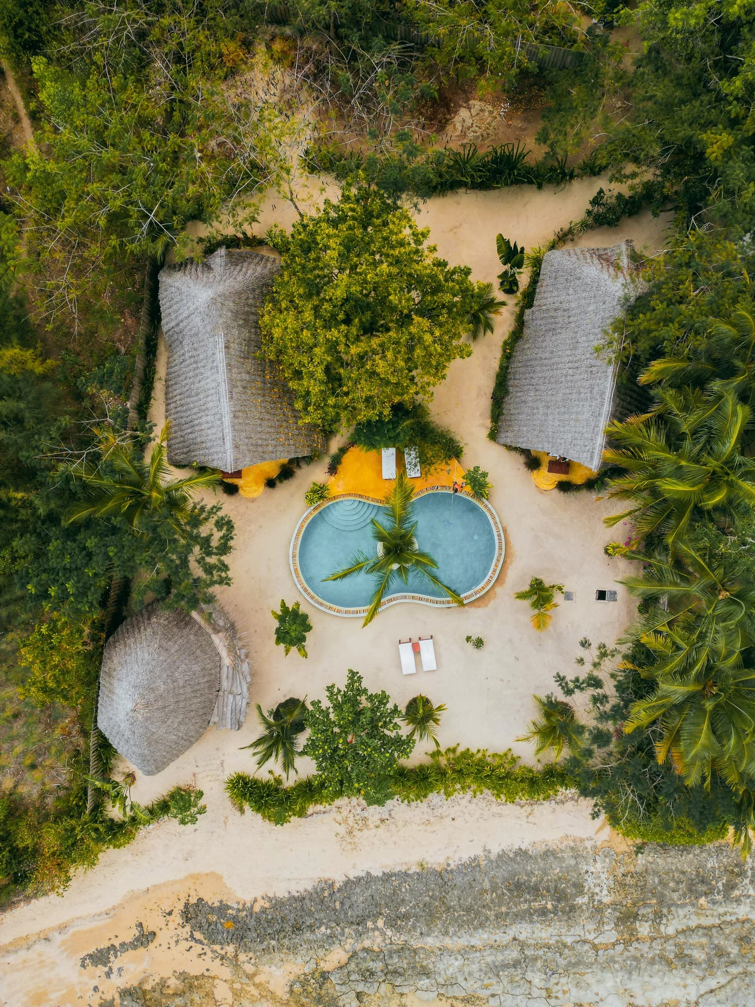 Top-down aerial view of Milele Villas, its pool and the tropical coastline