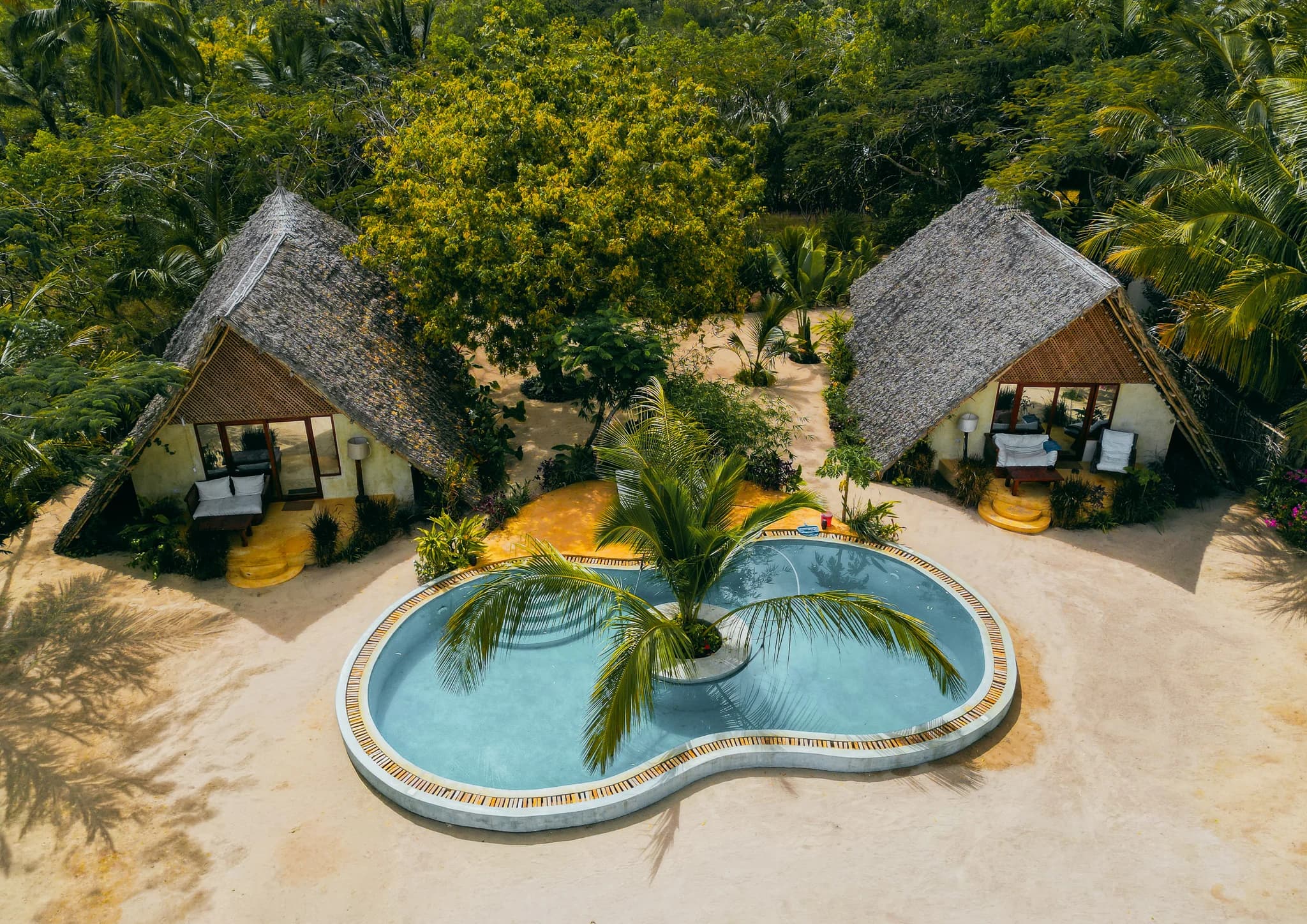 Aerial view of the pool and thatched villas surrounded by tropical gardens at Milele Villas