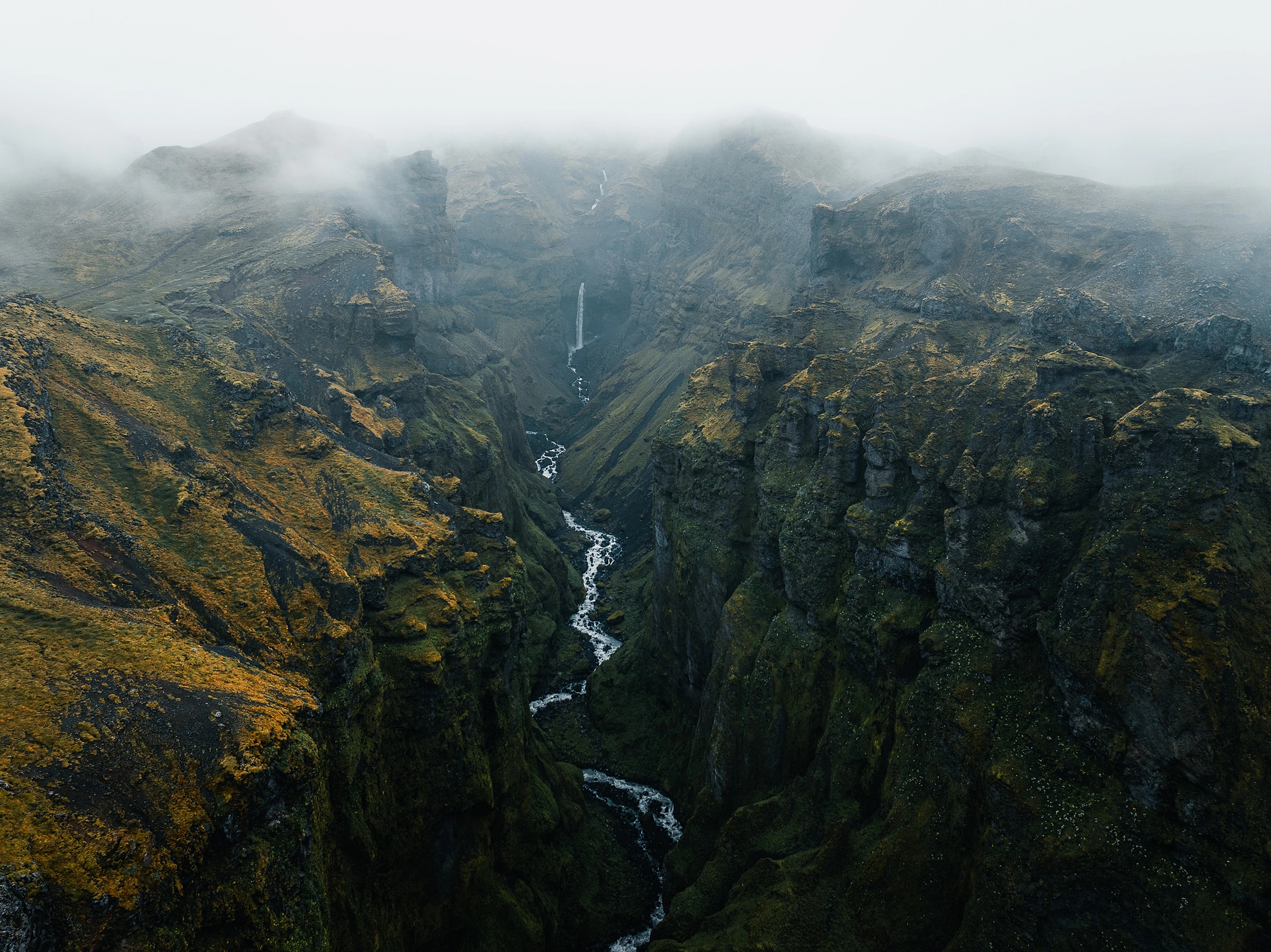 A misty canyon with a waterfall winding through moss-covered cliffs